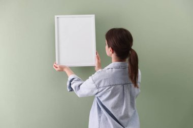 Yeşil duvarda boş bir çerçeve asılı kadın, arka manzara