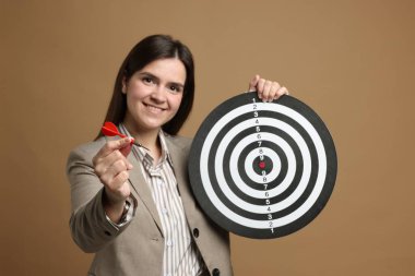 Hedef alınıyor. Dart tahtası ve bej arka planda oku olan gülümseyen iş kadını.