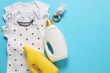 Açık mavi arka planda yumuşatıcı, oyuncak ve bebek kıyafetleri, düz yatak. Metin için boşluk