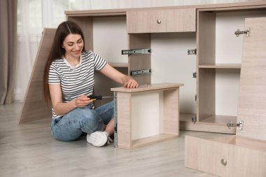 Gülümseyen kadın evde yerde tornavidayla mobilya monte ediyor.