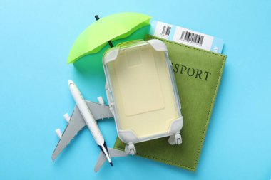 Seyahat sigortası. Uçak modeli, küçük şemsiye, pasaport, bavul ve açık mavi arka plan biletleri, düz yatış