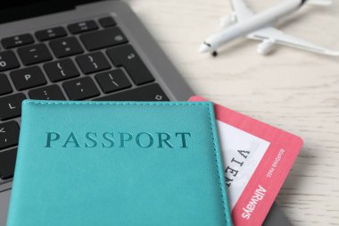 Pasaport, uçuş bileti, uçak modeli ve laptop beyaz ahşap masada, yakın plan.