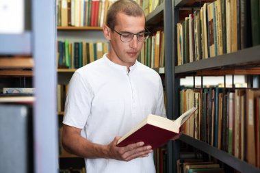 Halk kütüphanesinde rafların yanında kitap okuyan adam