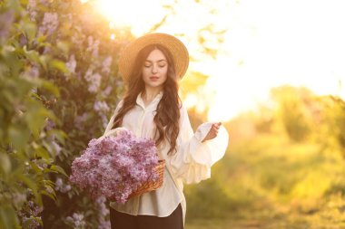 Güzel bir kadın, sabah çalıların yanında bir sepet leylak çiçeği taşıyor.