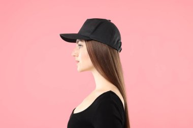 Pembe arka planda şık beysbol şapkalı güzel bir kadın.