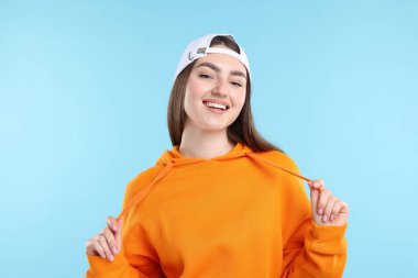 Açık mavi arka planda, şık beyzbol şapkalı, gülen kadın.