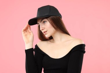 Pembe arka planda şık beysbol şapkalı güzel bir kadın.