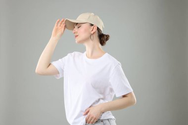 Gri arka planda şık beyzbol şapkalı güzel bir kadın.