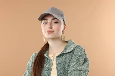 Bej arka planda şık bir beyzbol şapkası takmış güzel bir kadının portresi.