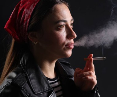 Bandanalı kadın siyah arka planda sigara içiyor, yakın plan.