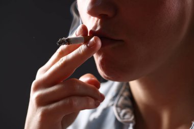 Arka planda sigara içen tişörtlü bir kadın, yakın plan. Kötü alışkanlık.