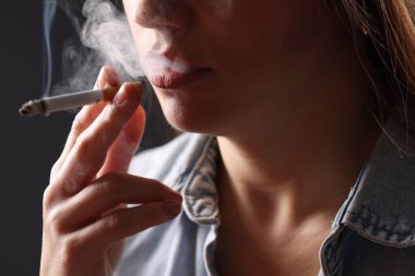 Arka planda sigara içen tişörtlü bir kadın, yakın plan. Kötü alışkanlık.