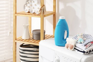 İçinde kumaş yumuşatıcı, bebek kıyafetleri ve çamaşır makinesinde oyuncak olan bir şişe.