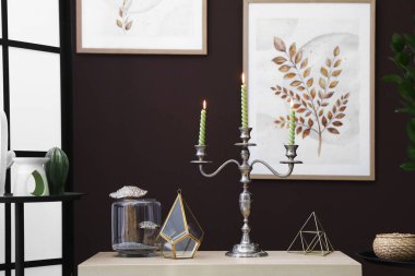 Kahverengi duvarın yanındaki dolapta yanan mumlar ve dekorlar olan zarif bir şamdan.