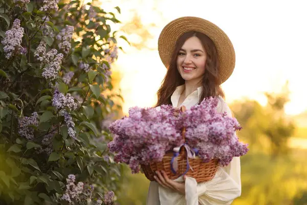Gülümseyen kadın sabah çalıların yanında bir sepet leylak çiçeğiyle
