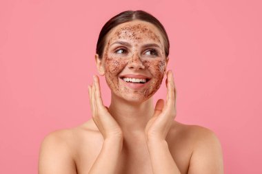 Gülümseyen kadın yüzünü pembe arka planda ovuşturuyor.