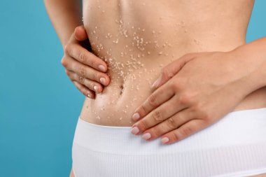 Göbeğini açık mavi arka planda ovuşturan kadın, yakın plan.