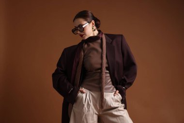 Kahverengi arka planda şık giyinmiş genç bir kadın.