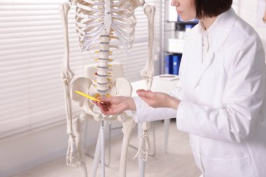 Doktor klinikteki insan iskeleti parçalarına işaret ediyor.