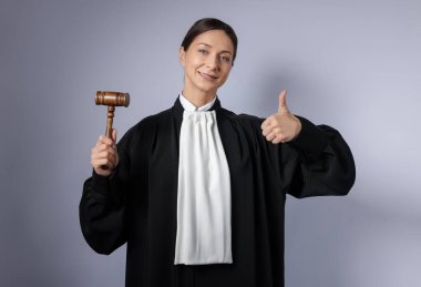 Aydınlık arkaplanda başparmak gösteren çekiçli yargıç