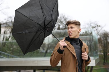 Kırık şemsiyeli bir adam açık havada yağmur altında rüzgarla savaşıyor.