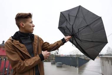 Kırık şemsiyeli bir adam açık havada yağmur altında rüzgarla savaşıyor.