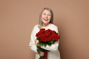 Bej arka planda bir buket gülle gülümseyen kadın.