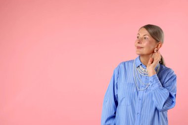 Üst düzey kadın pembe arka planda zarif inci takılar takıyor, mesaj için yer var.