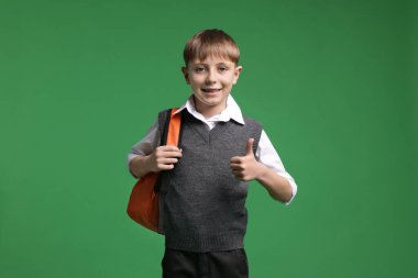 Sırt çantalı mutlu okul çocuğu yeşil arka planda baş parmak gösteriyor.