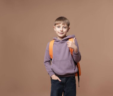 Sırt çantalı yakışıklı okul çocuğu kahverengi arka planda baş parmak gösteriyor.