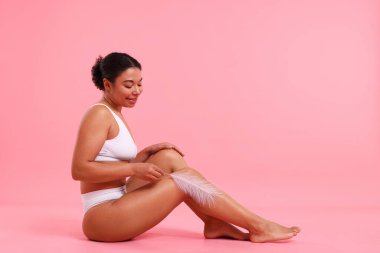 İç çamaşırlı kadın pembe arka plandaki epilasyon işleminden sonra pürüzsüz cildini gösteriyor.