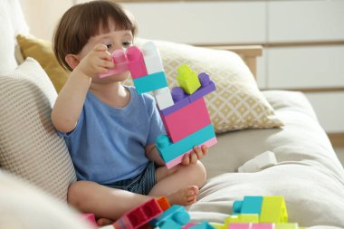 Evdeki kanepede tuğlalarla oynayan şirin bir çocuk.