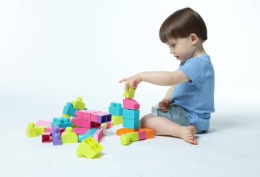 Beyaz arka planda tuğlalarla oynayan sevimli küçük çocuk.