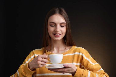 Kahverengi arka planda bir fincan kahveyle gülümseyen kadın.