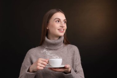 Kahverengi arka planda bir fincan kahveyle gülümseyen kadın.