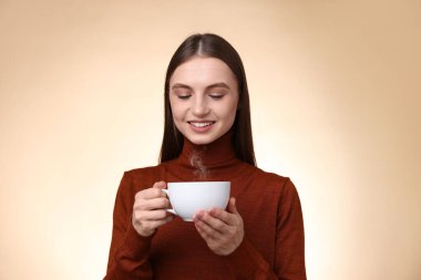 Bej renkli arka planda bir fincan kahveyle gülümseyen kadın