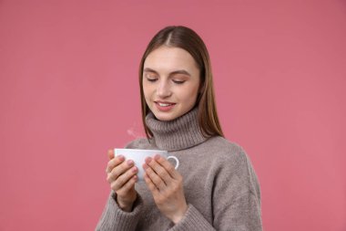 Pembe arka planda bir fincan kahveyle gülümseyen kadın.