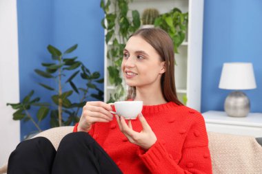 Evdeki kanepede bir fincan kahveyle gülümseyen kadın.