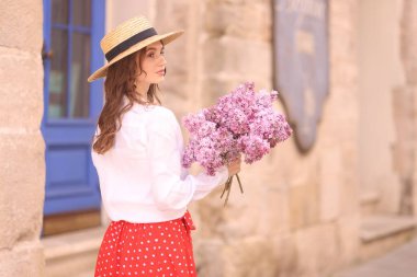 Şapkalı güzel bir kadın, bina yakınlarında bir demet leylak çiçeğiyle. Metin için boşluk
