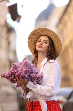 Şapkalı güzel bir kadın ve açık havada bir demet leylak çiçeği.