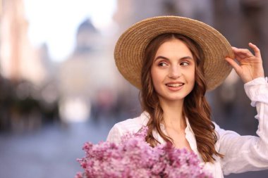 Bulanık arka planda bir demet leylak çiçeğiyle şapkalı gülümseyen kadın. Metin için boşluk