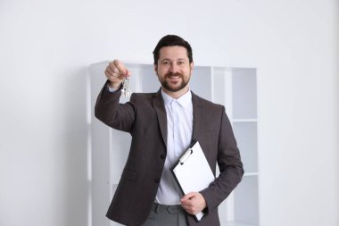 Emlakçının elinde evin anahtarı, anahtarlık ve pano var.