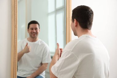 Kapalı alanda aynanın yanında baş parmağını gösteren yakışıklı adam.