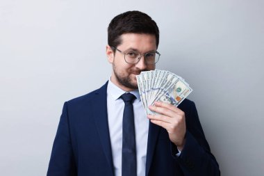 Açgözlü bankacı, gri arka planda dolar banknotlarını kokluyor.