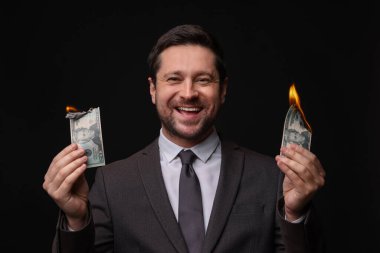 Siyah arka planda dolarları yakan mutlu açgözlü bankacı.