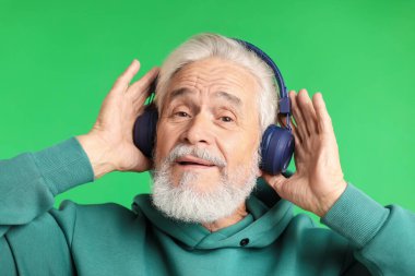 Yeşil arka planda kulaklıklı yaşlı bir adam.