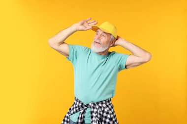 Turuncu arka planda şık giyinmiş yaşlı bir adam.