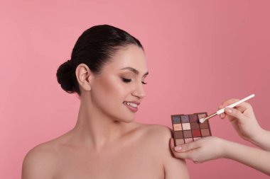 Göz falı paleti olan makyaj sanatçısı, pembe arka planda fırça ve gülümseyen kadın, yakın plan.