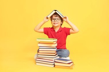 Turuncu arka plan hakkında çok farklı kitapları olan bir çocuk.