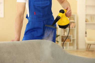 Temizlikçi kanepeyi evde buharlı temizleme makinesiyle temizliyor.
